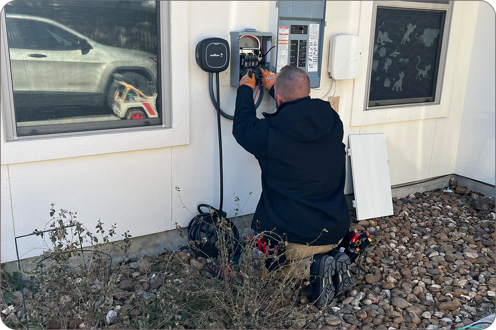 Eddie Burton is on his knees placing an EV charger next to a car on a white wall.