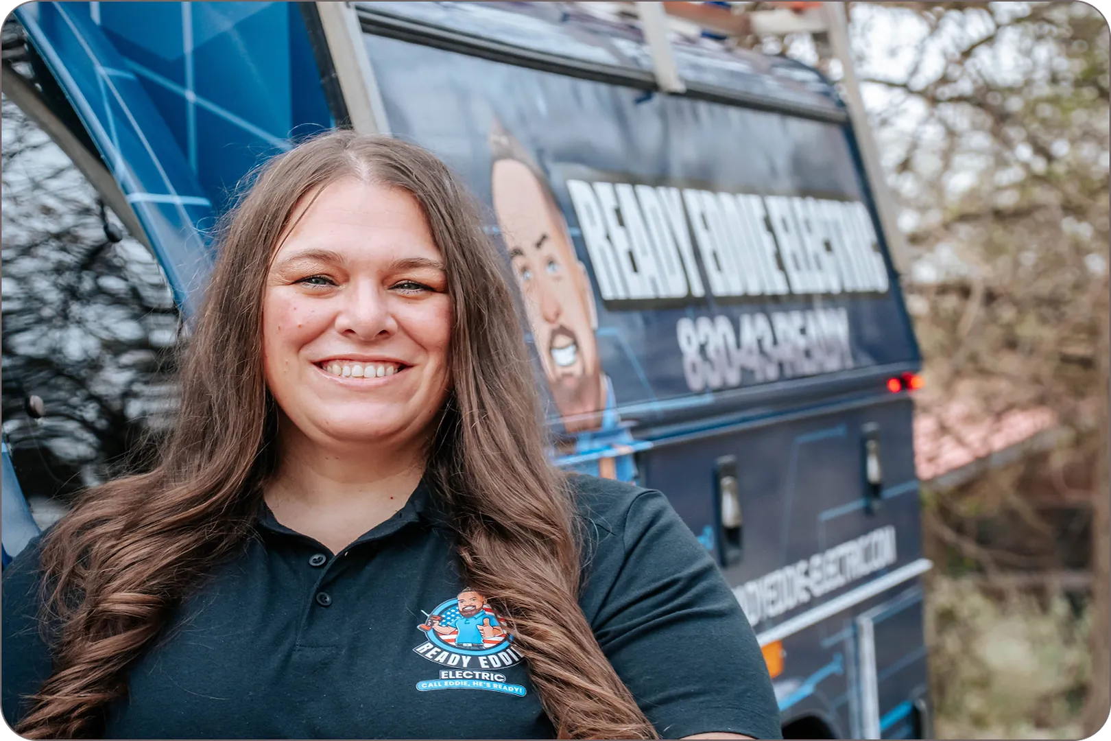 Eddie Burton’s wife, wearing a company polo, stands in front of a blue work van.