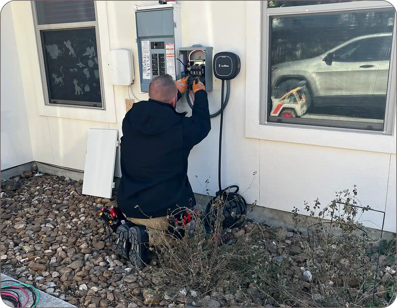 Eddie Burton is on his knees placing an EV charger next to a car on a white wall.