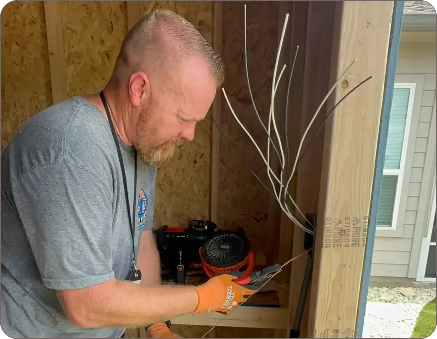Eddie Burton carefully works on electrical wiring in a wooden shed, wearing protective gloves.