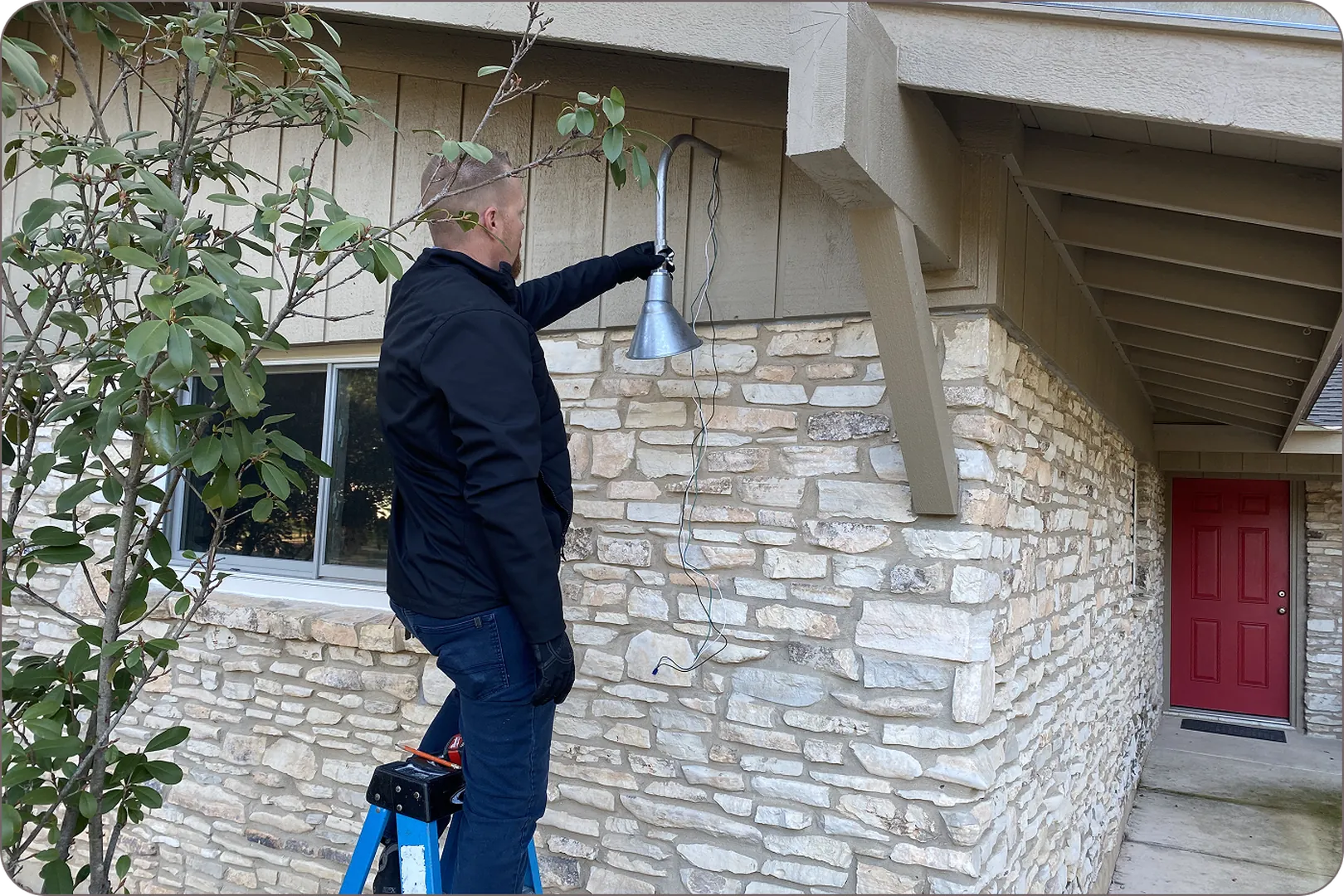 Eddie Burton is using a blue ladder to adjust a silver outdoor light.